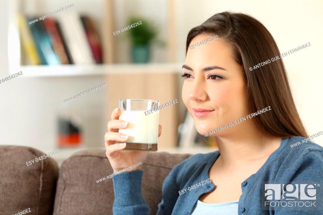 Stock Photo: Relaxed woman holding a glass of milk sitting on a couch in the living room at home.