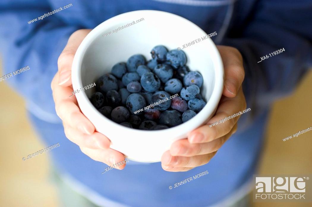 Stock Photo: A boy holds a small white bowl containing freshly picked blueberries.