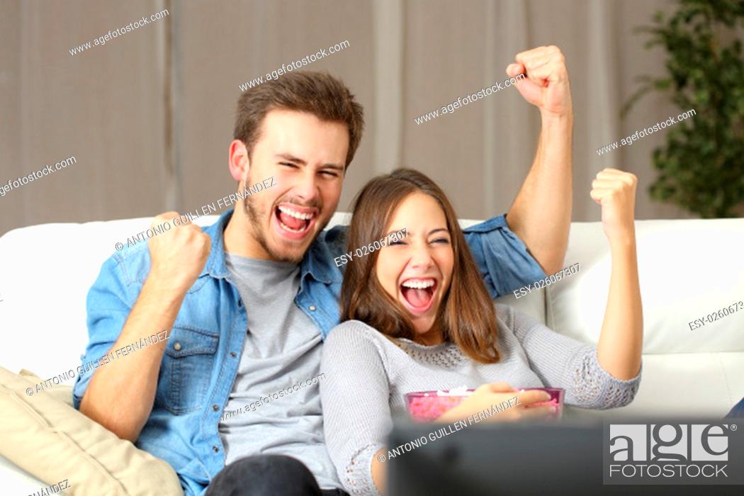 Stock Photo: Euphoric couple watching tv sitting on a couch at home.