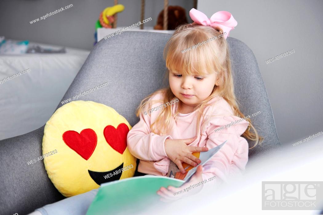 Stock Photo: Portrait of blond little girl sitting in arm chair looking at picture book.