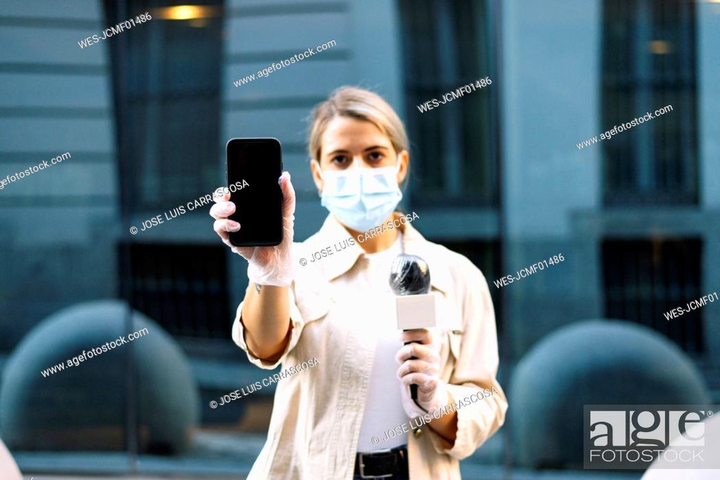 Stock Photo: Female journalist wearing mask showing smart phone while standing in city.