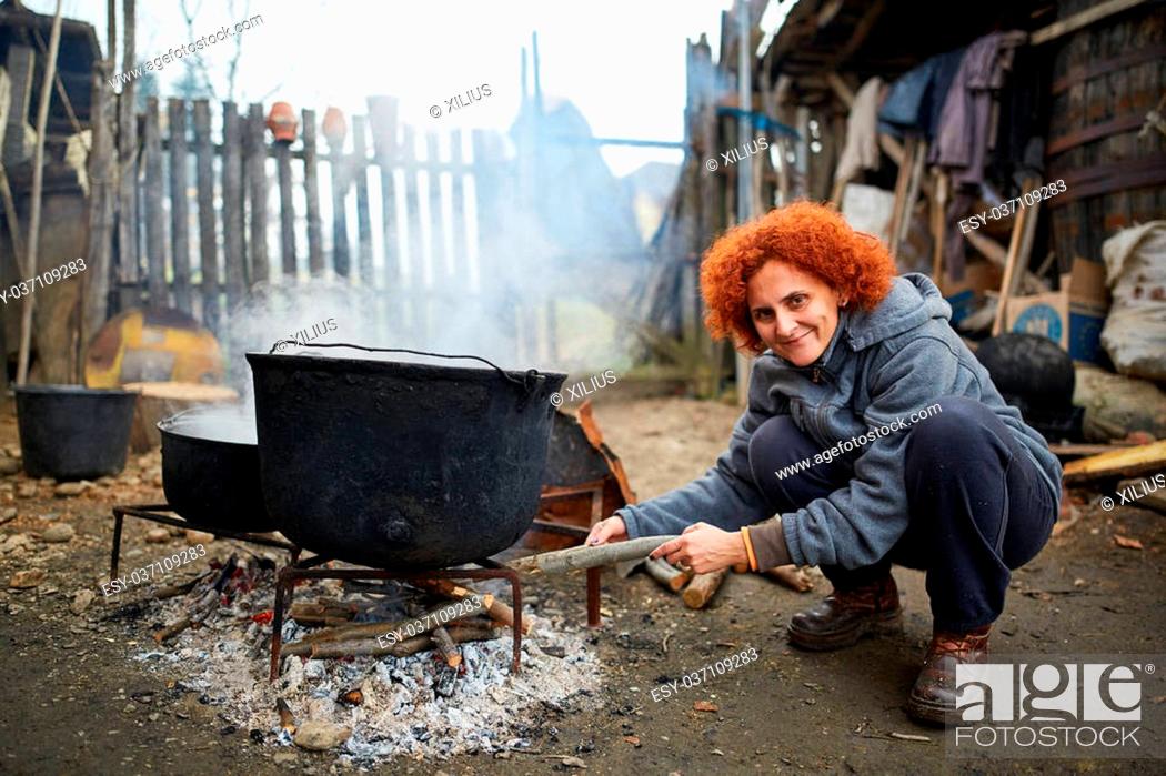 Stock Photo: Curly haired peasant woman boiling water in very big cast iron pots.