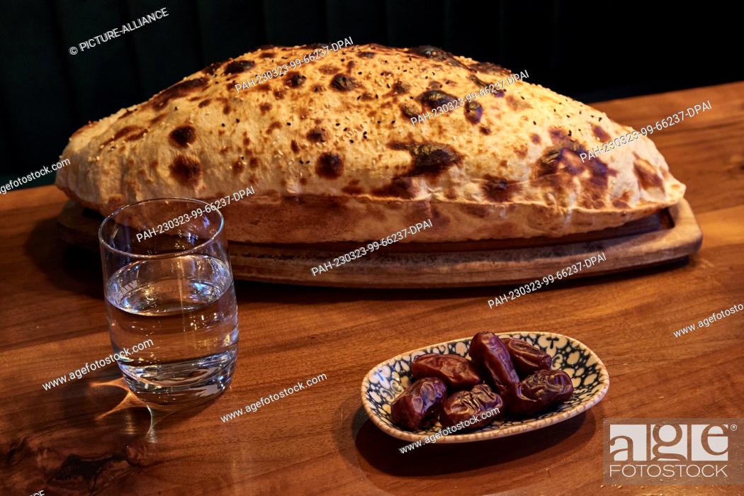 Stock Photo: 23 March 2023, Hamburg: A glass of water, a bowl of dates and the Sisme Ekmek stone-baked bread are on the table at the Pamukkale Köz restaurant.