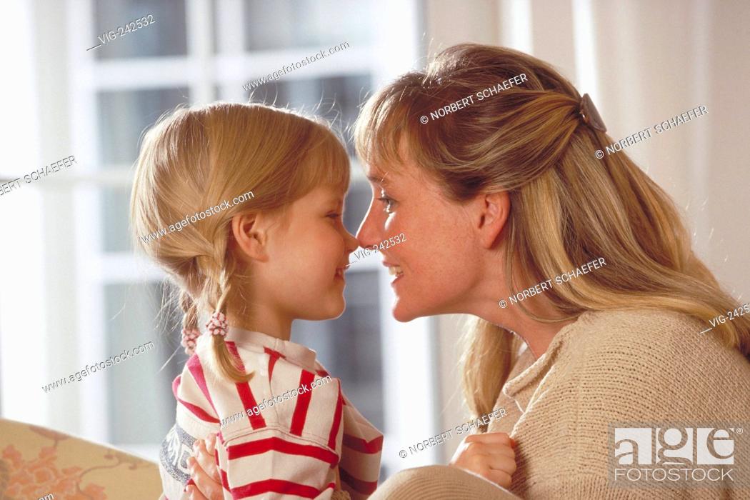 Stock Photo: portrait, indoor, bright dressed blond woman and her 6-year-old blond daughter wearing a red-white shirt sit on the sofa smooching  - GERMANY, 02/03/2005.