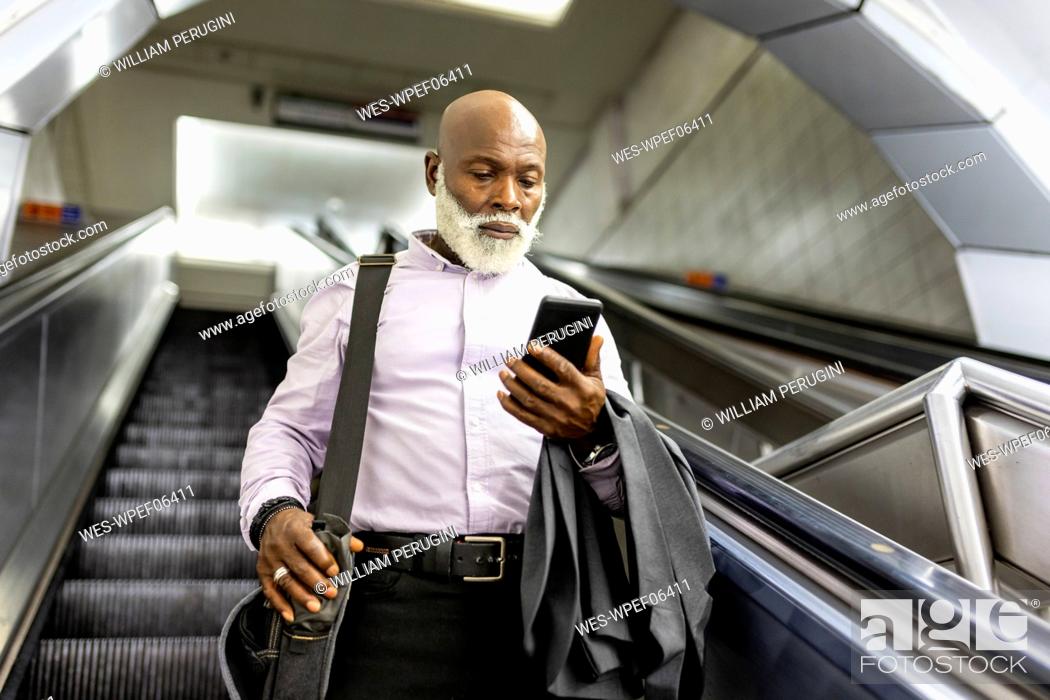 Stock Photo: Senior commuter with laptop bag using smart phone on escalator.
