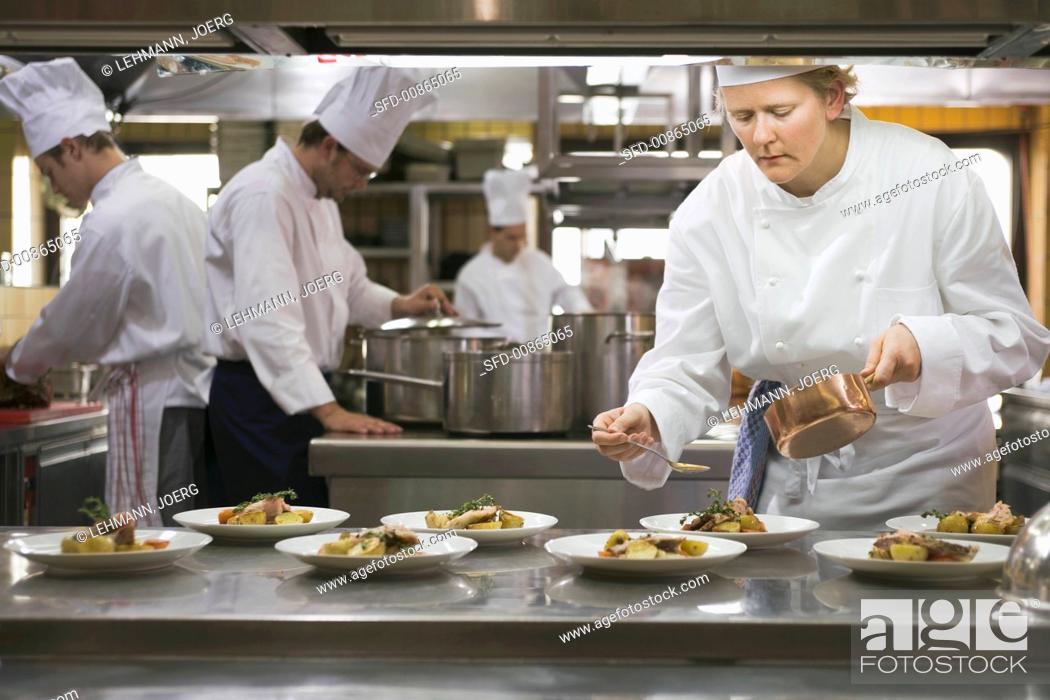 Stock Photo: Female chef spooning sauce over main courses.