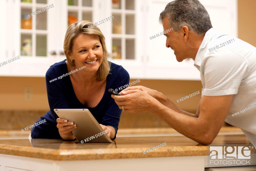 Stock Photo: Caucasian couple using digital tablet and cell phone at kitchen counter.