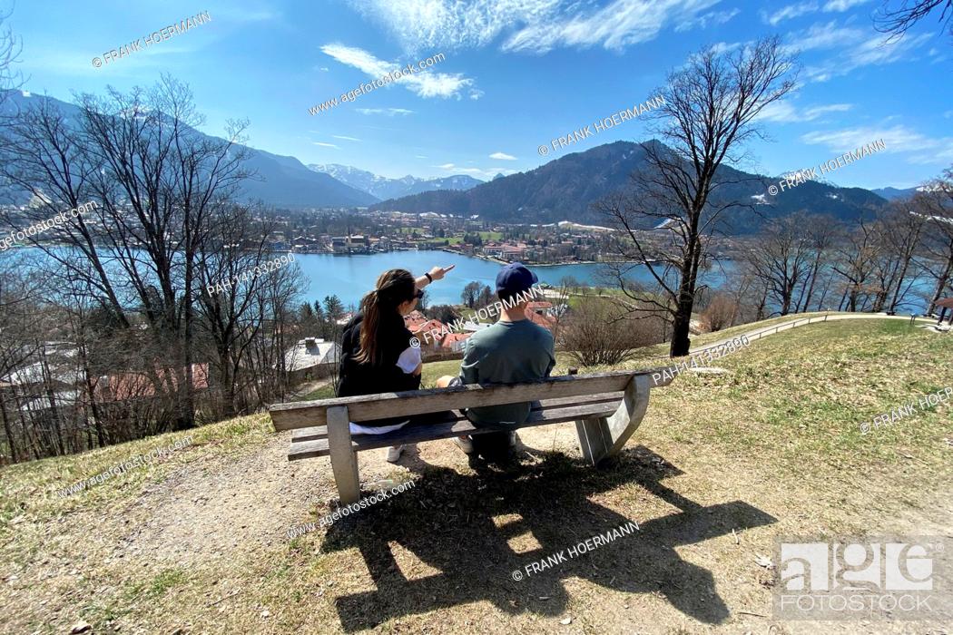 Stock Photo: Young couple takes a rest on a bench. Hikers on the Hoehenweg over the Tegernsee with a view of Rottach Egern on April 1st, 2021.