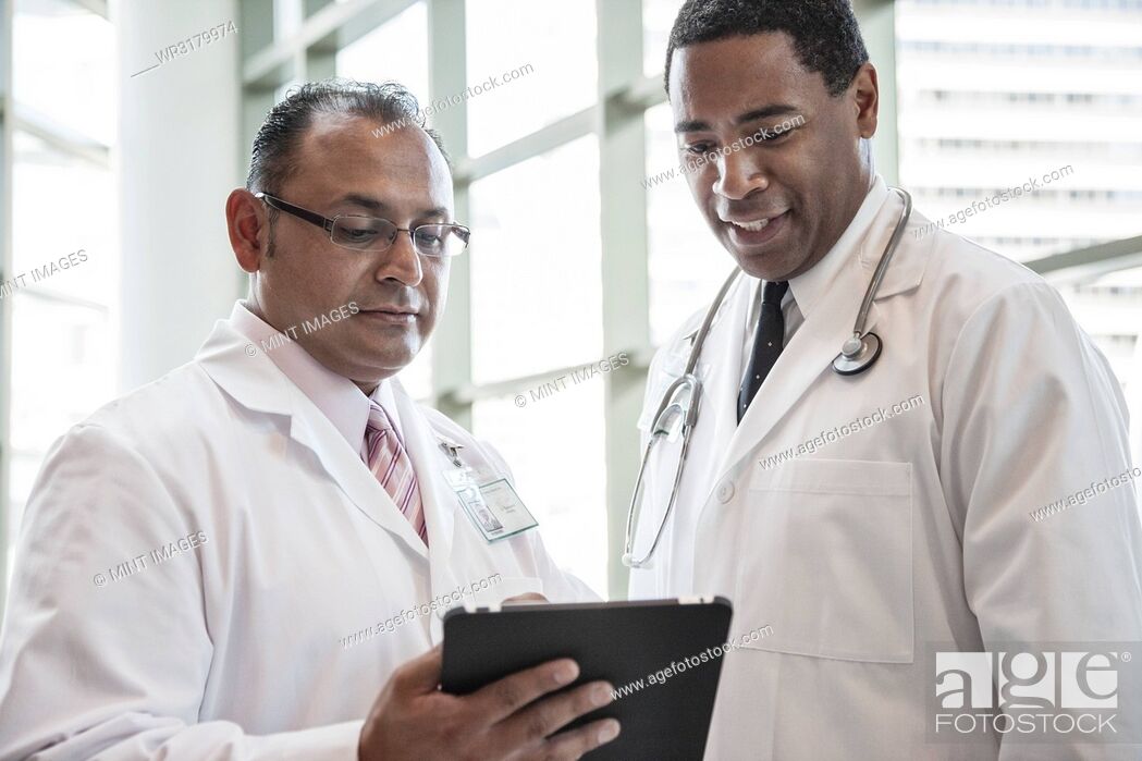 Stock Photo: Black and Hispanic male doctors discussing a case in a hospital hallway.