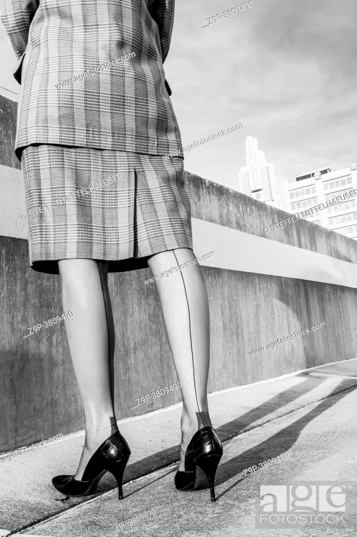 Photo de stock: Back view of woman wearing a plaid business suit , Cuban heeled nylon seamed stockings, and vintage crocodile patterned stiletto pumps standing on the top deck.