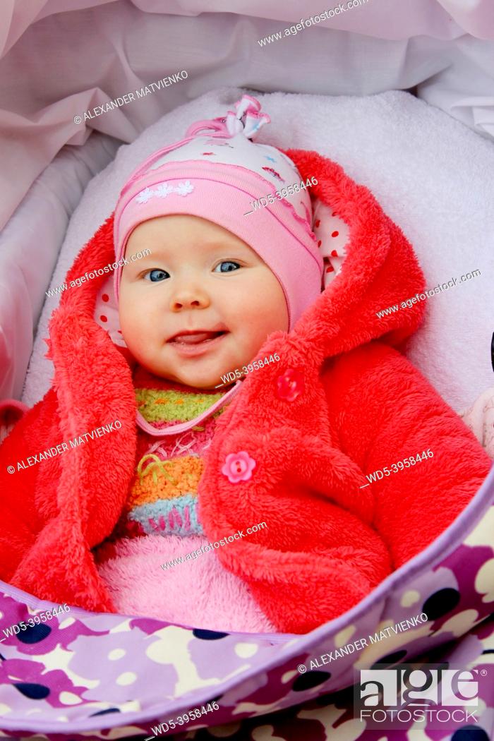 Stock Photo: little baby in red suit smiling in perambulator. Happy baby laying in pram. Childish face close up.