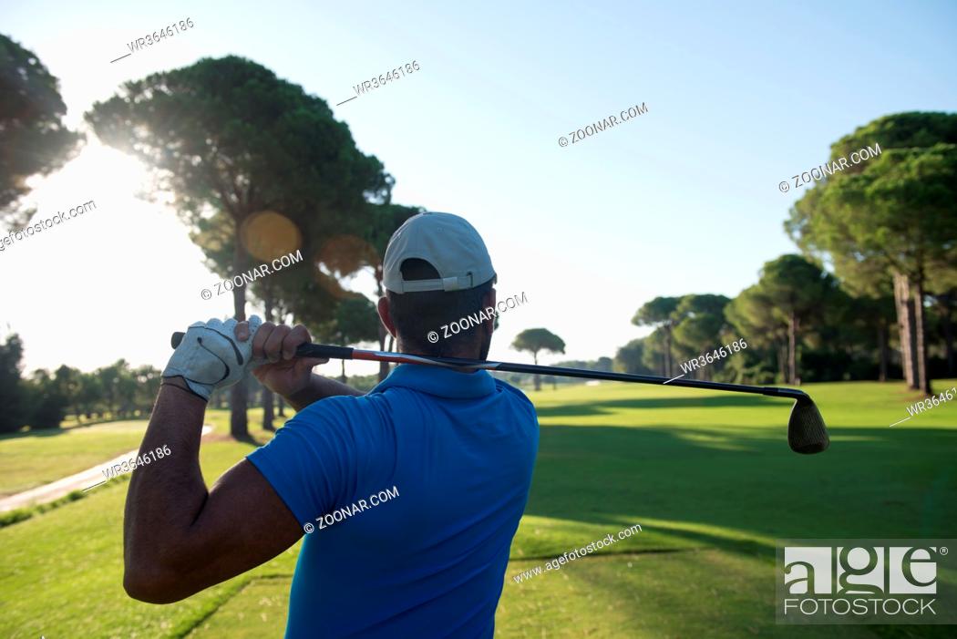 Stock Photo: golf player hitting shot with club on course at beautiful morning with sun flare in background.
