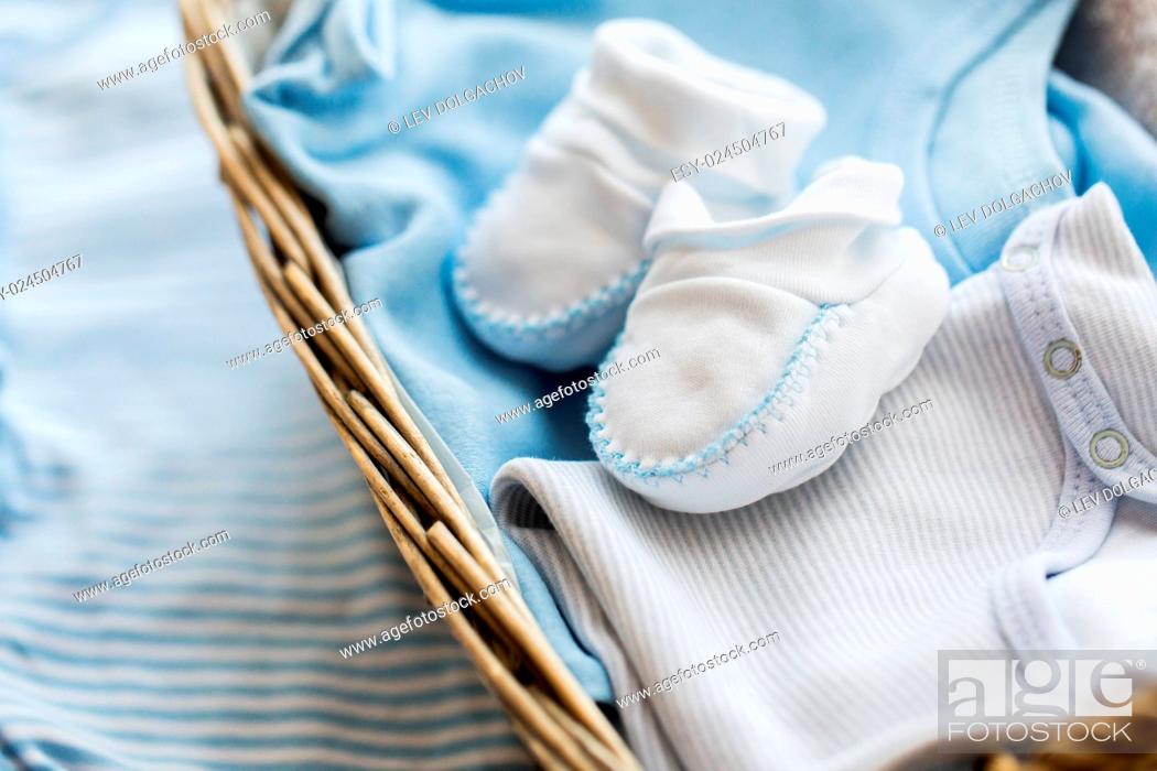 Stock Photo: clothing, babyhood, motherhood and object concept - close up of white baby bootees with pile of clothes and towel for newborn boy in basket on table.