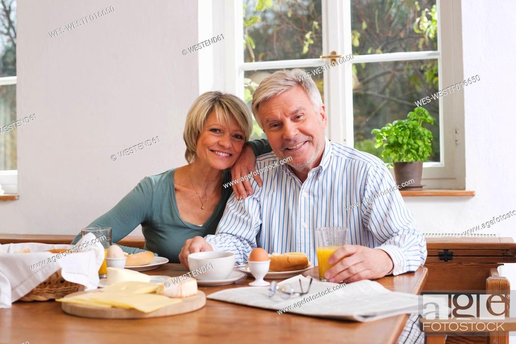 Stock Photo: Germany, Kratzeburg, Senior couple having breakfast, smiling, portrait.