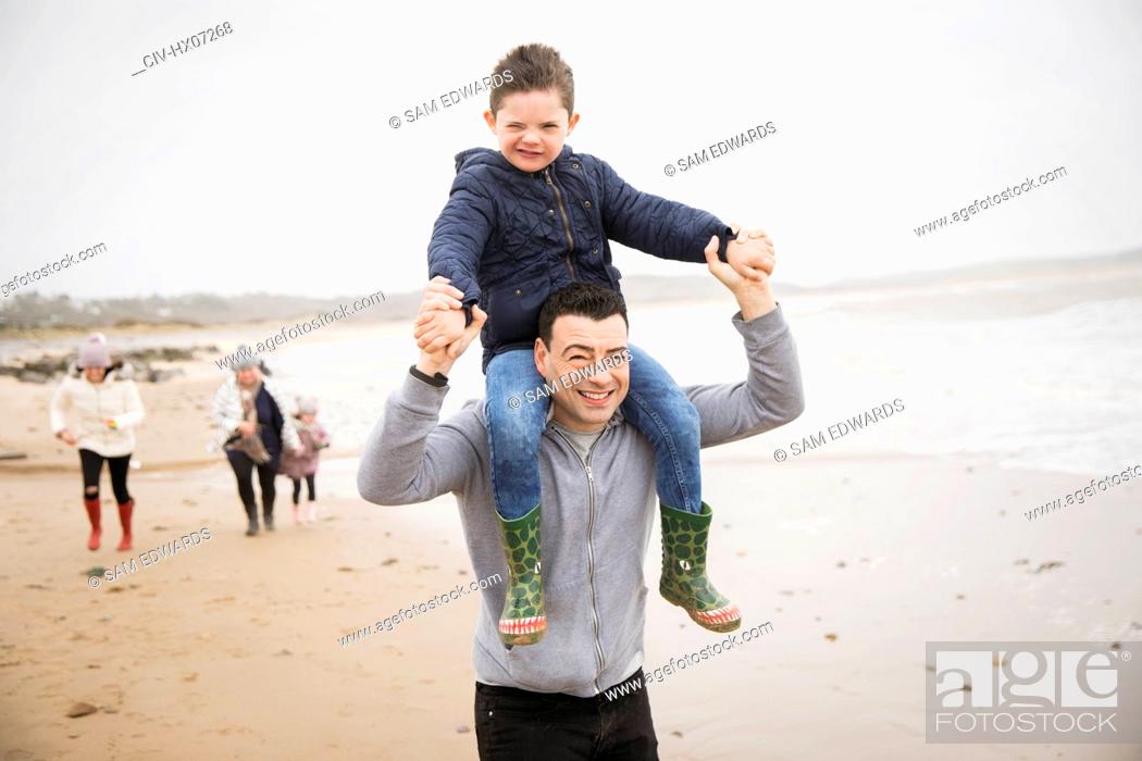 Stock Photo: Portrait playful father carrying son on shoulders on winter beach.