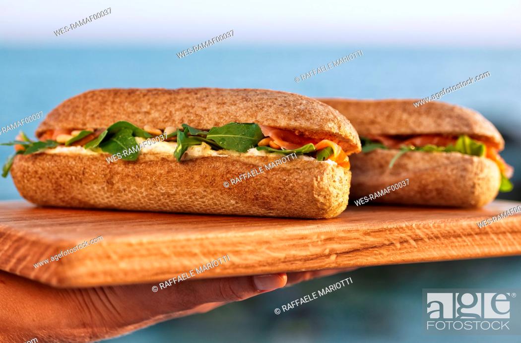 Stock Photo: Woman's hand holding wooden board with two Salmon sandwiches.