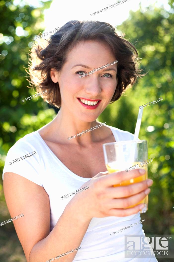Stock Photo: Happy woman with orange juice standing by trees.