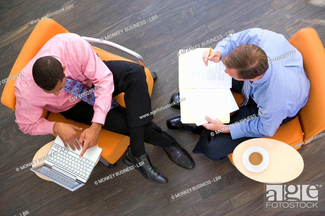 Stock Photo: Two businessmen sitting indoors with coffee laptop and folder.