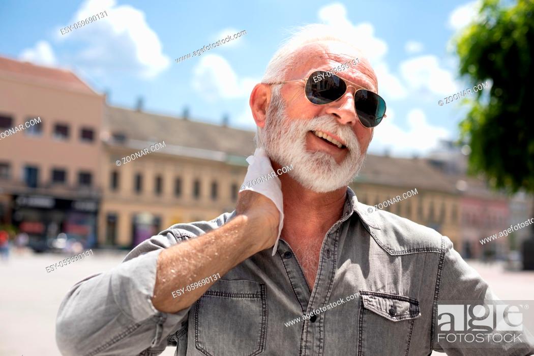 Stock Photo: Old man cleaning neck and sweat with wet wipes on street on hot summer day, blurred urban city background.