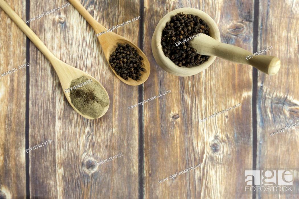 Stock Photo: two wooden spoons with black peppercorns and ground with wooden mortar filled with pepper on old wooden table from above. Top view.