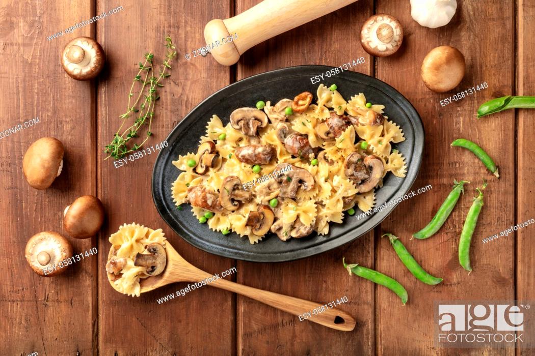 Stock Photo: Mushroom and cheese pasta. Farfalle with cremini and green peas, shot from the top with ingredients on a dark rustic wooden background.