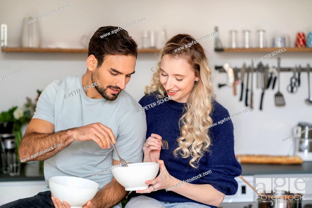 Photo de stock: Smiling young woman sharing food with boyfriend in kitchen at home.
