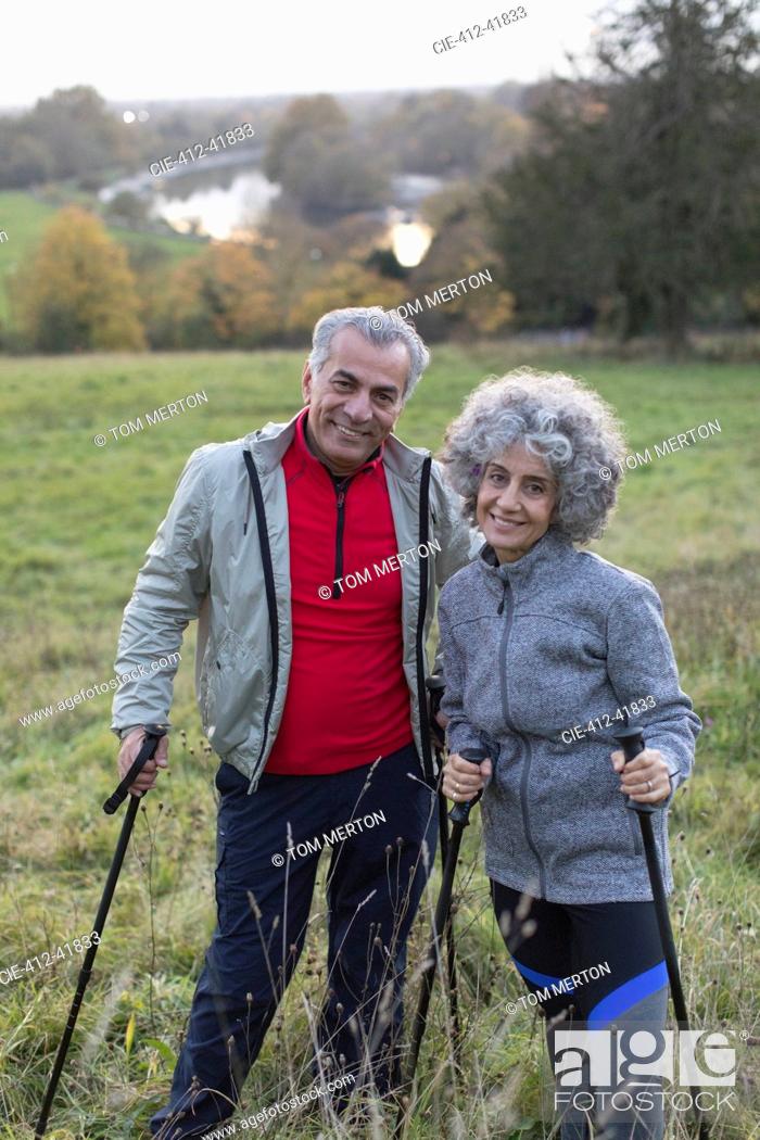 Stock Photo: Portrait confident active senior couple hiking with poles in rural field.