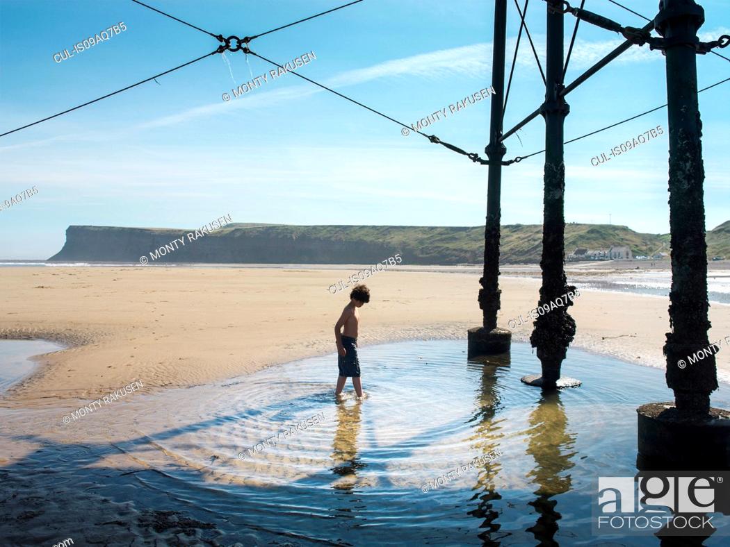 Stock Photo: Boy paddling in water under pier at beach.