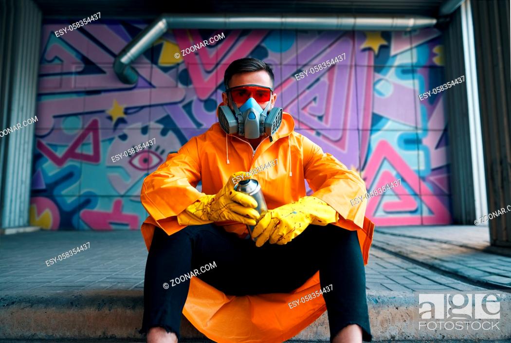 Stock Photo: Graffiti painter rest near the wall with his paintings looking to camera. Street art concept.