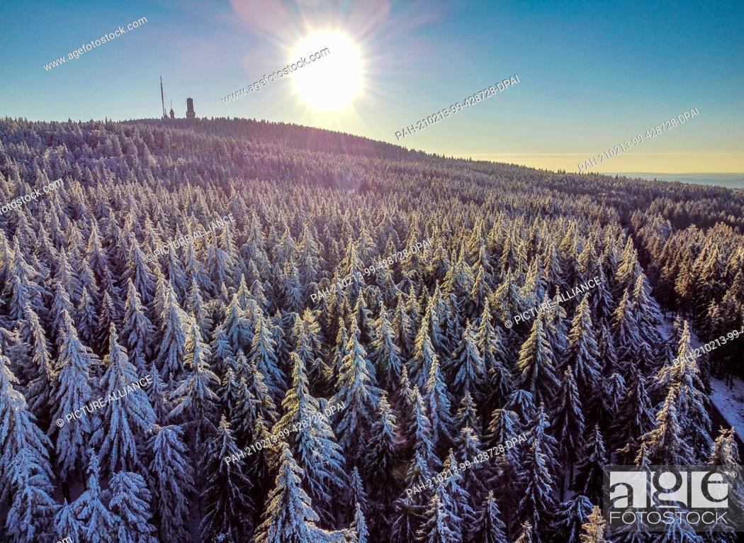 Stock Photo: 13 February 2021, Hessen, Sandplacken: The sun sets behind the trees covered with snow and ice at the Feldberg in Taunus (aerial view with a drone).