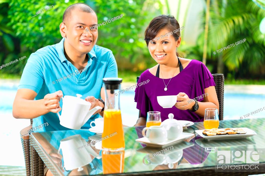 Stock Photo: Asian couple having coffee on the porch in front of their home, in the background a tropical garden.
