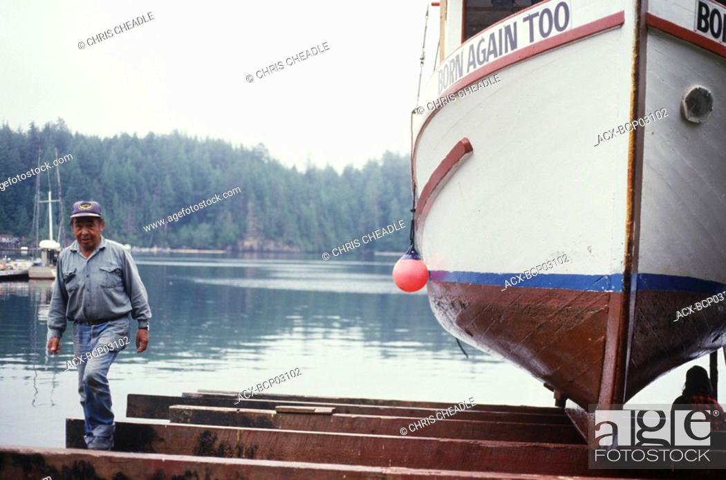 Stock Photo: Kyuquot, first nations fisher examines boat hull, Vancouver Island, British Columbia, Canada.