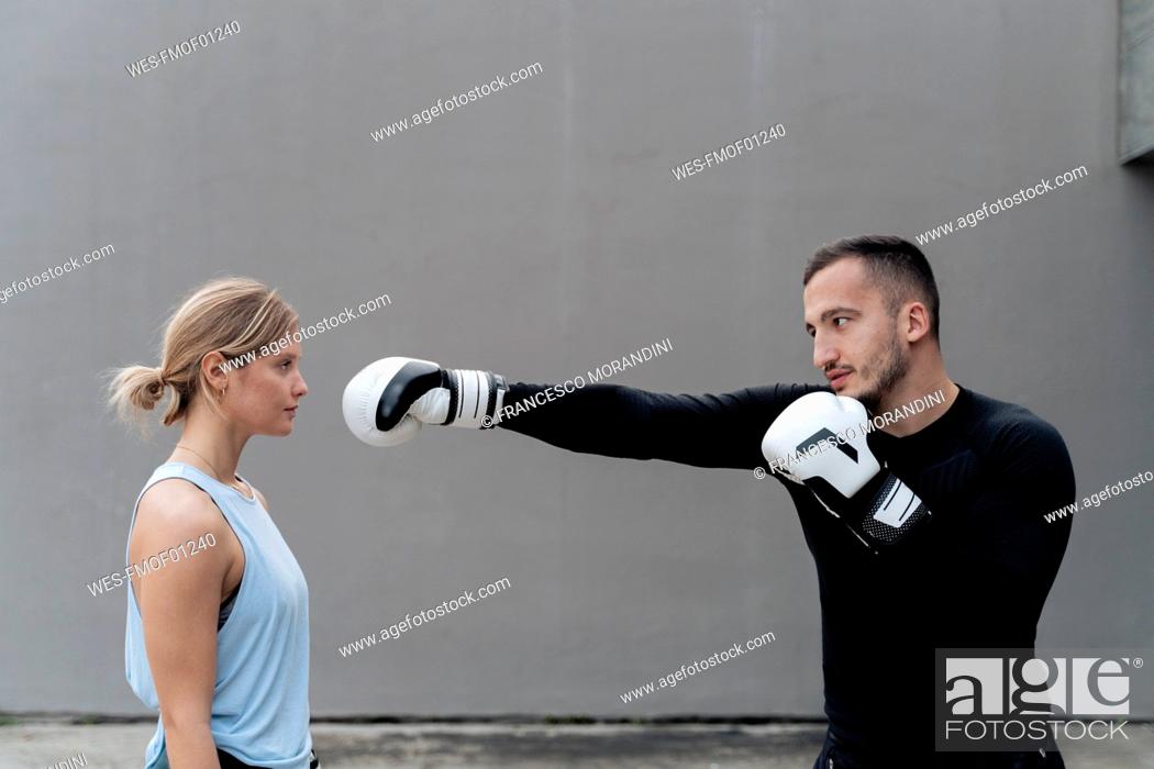 Stock Photo: Sportsman practicing boxing with woman while standing against wall.