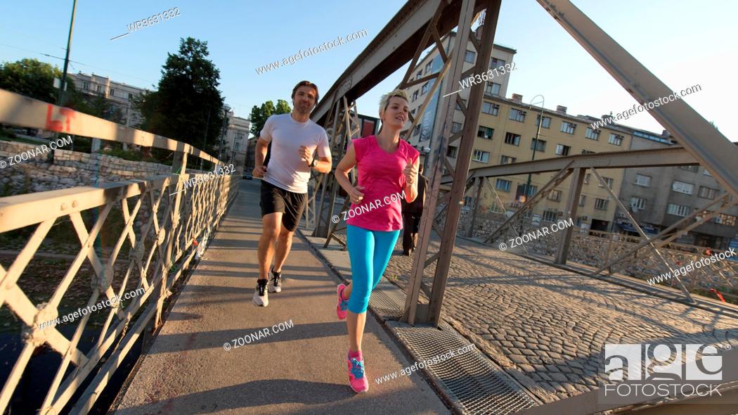 Stock Photo: healthy mature couple jogging in the city at early morning with sunrise in background.