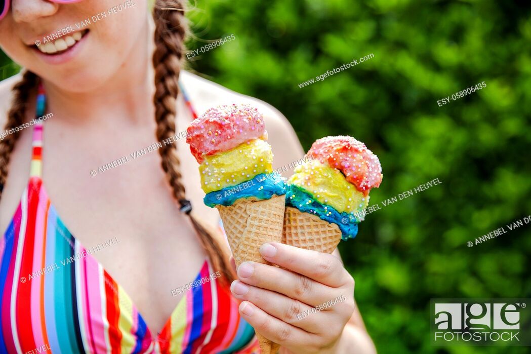 Stock Photo: Beautiful girl holding two colorful ice cream with sprinkles wearing a rainbow colored swimsuit in the summer, pink sunglasses and braids happy vacation.
