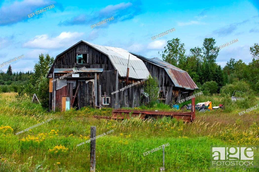 Stock Photo: A wide angle view of a dilapidated farm building. Neglected wood barn in a state of disrepair surrounded by rural farmland, with copy space to right.