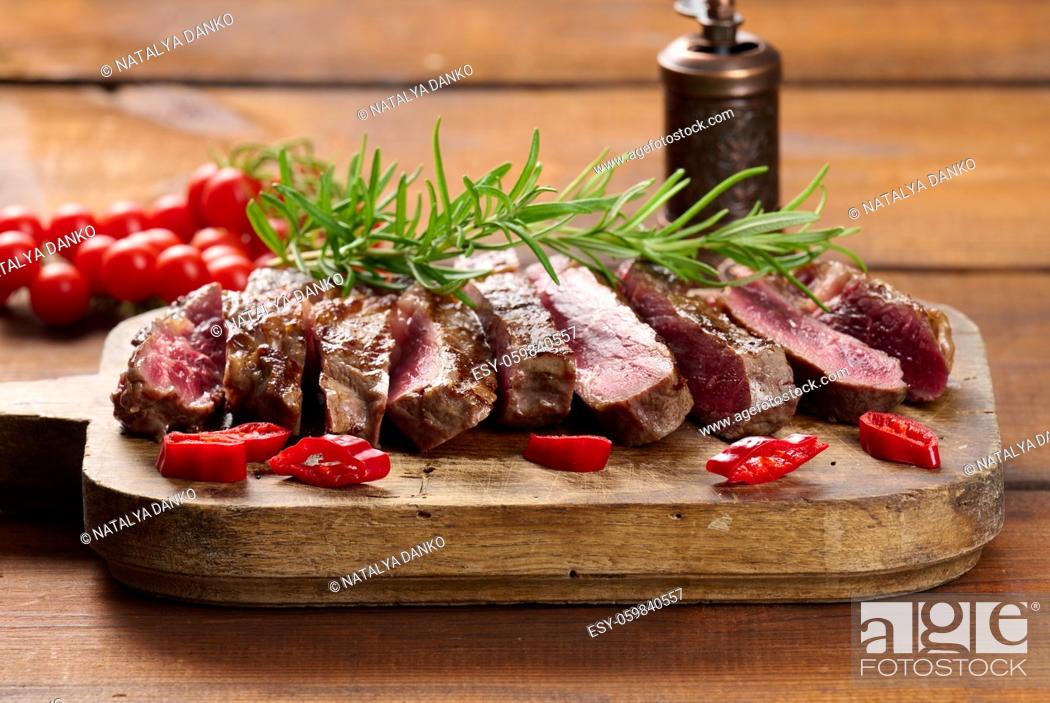 Photo de stock: roasted piece of beef ribeye cut into pieces on a vintage brown chopping board. Well done. Appetizing steak.