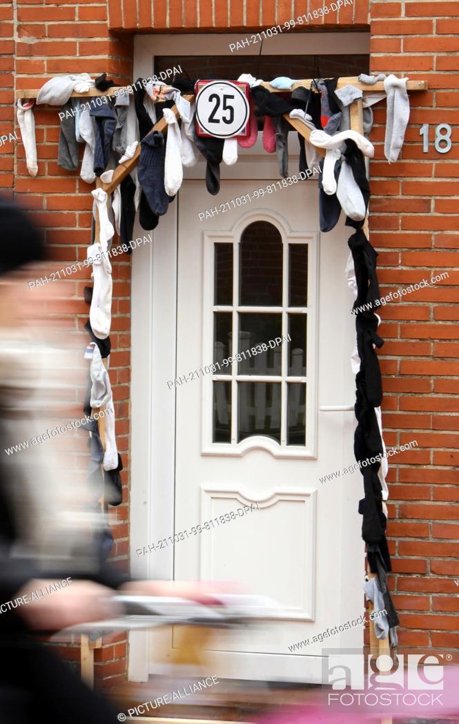 Stock Photo: 19 October 2021, Lower Saxony, Juist: On the car-free island of Juist, a large 25 surrounded by many socks is attached to a wooden scaffold at the entrance to a.