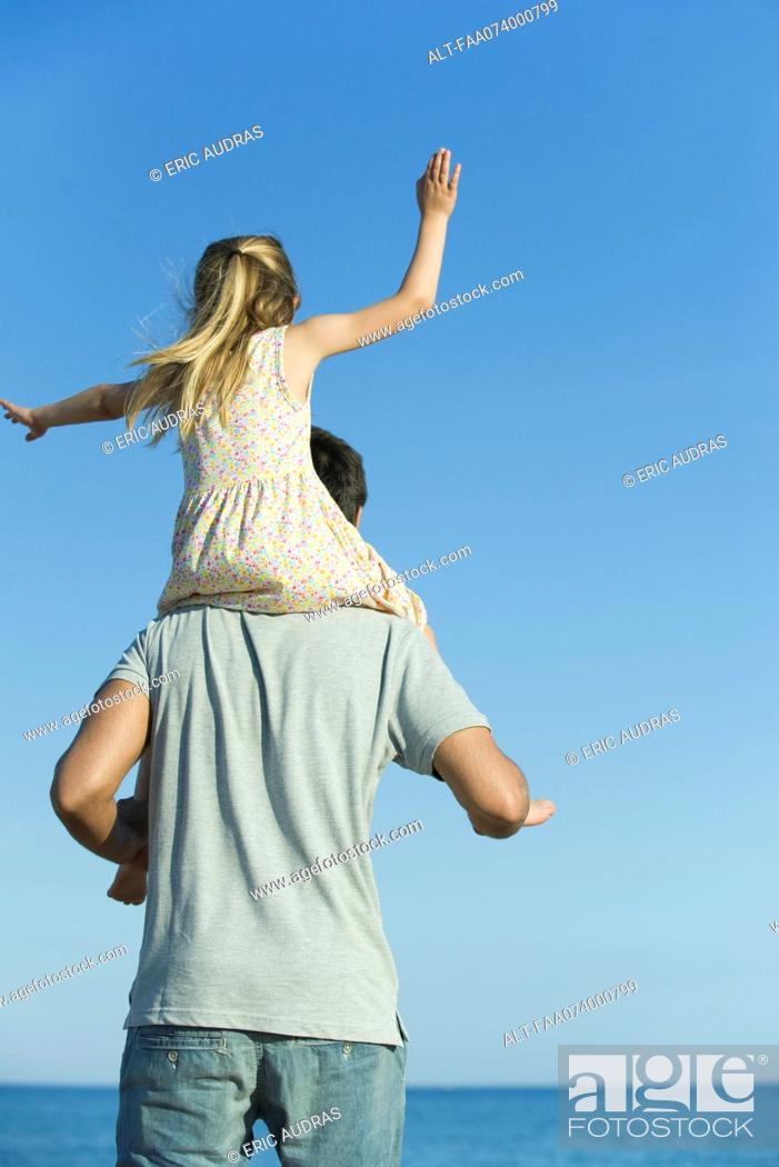 Photo de stock: Father carrying daughter on his shoulders, rear view.