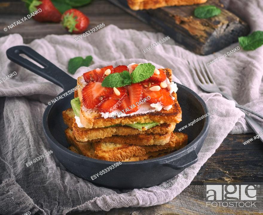 Imagen: pile of French toast from white bread with cottage cheese, strawberries in a black cast-iron round frying pan with a handle on a gray wooden table.