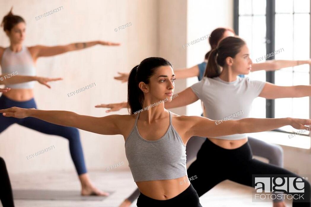 Stock Photo: Indian girl and diverse group of young people practicing yoga lesson doing Warrior II exercise, Virabhadrasana 2 pose, working out, indoor close up.