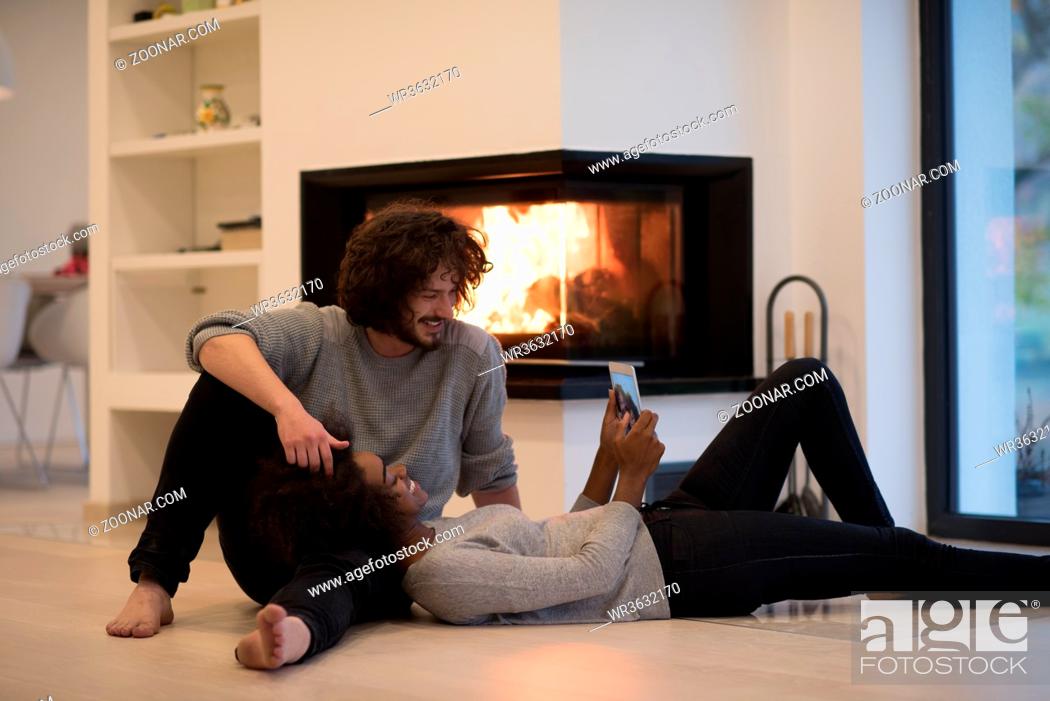 Stock Photo: beautiful young multiethnic couple using tablet computer on the floor of their luxury home in front of fireplace at autumn day.
