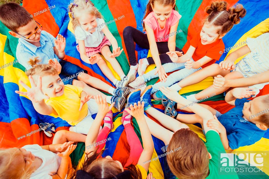 Stock Photo: Kids holding hands together sitting on rainbow parachute, children team-work concept.