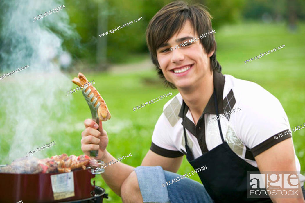 Stock Photo: Young man holding grilled sausage, smiling, close-up.
