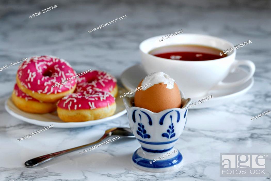 Stock Photo: Boiled egg with tea and donuts in the background, breakfast time.