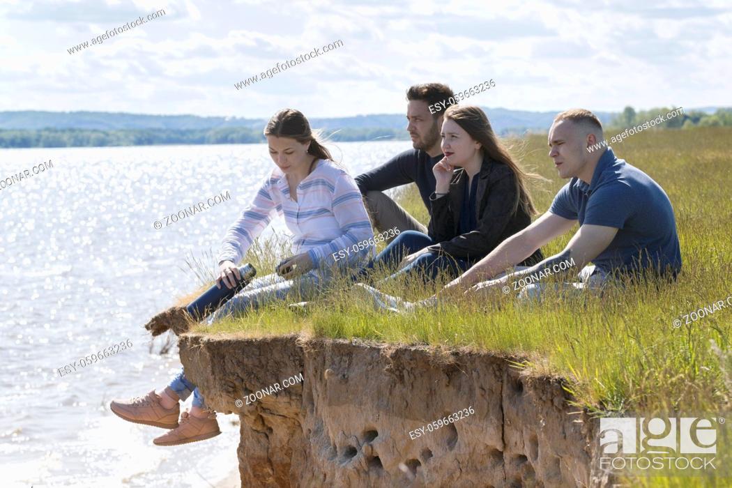 Stock Photo: Happy friends having fun on the hill over the river enjoying recreation and talking, horizontal.