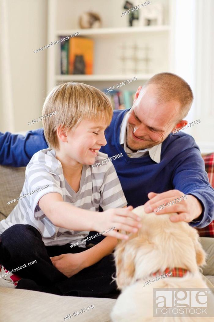 Stock Photo: Father and son in a couch patting a dog, Sweden.