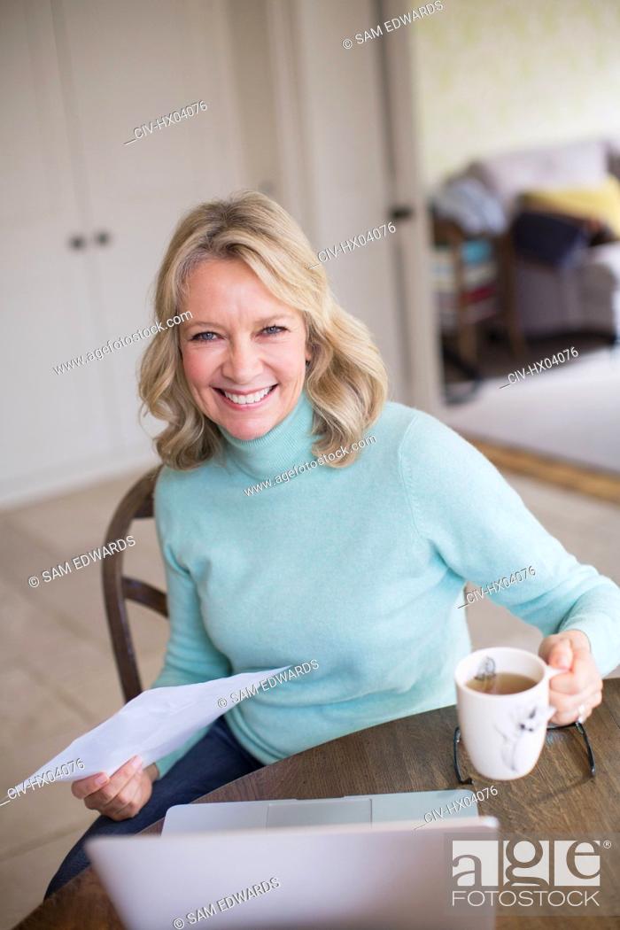 Stock Photo: Portrait smiling, confident female freelancer working at laptop and drinking tea at home.