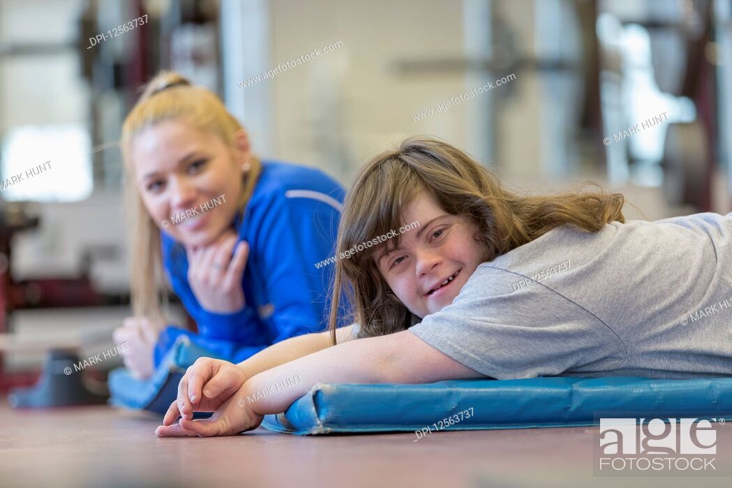 Stock Photo: Young woman with Down Syndrome working out with her trainer on a exercise mat in gym.