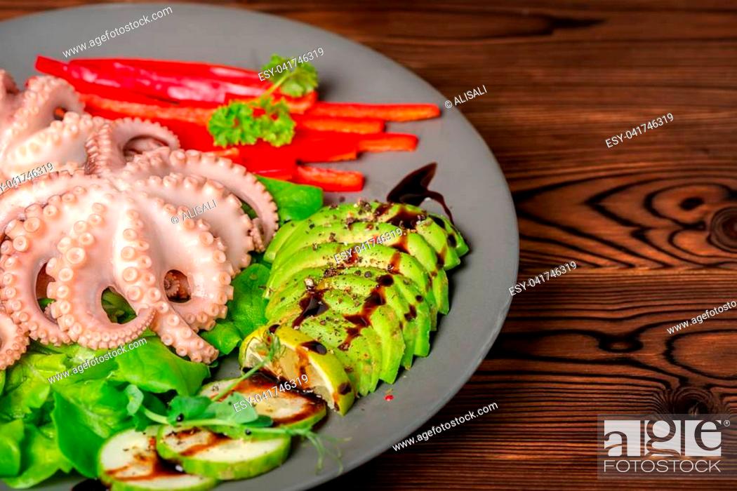 Photo de stock: octopus served with sliced avocado and sauce, lettuce, red pepper, lime, cucumber and sprig of pea leaves on plate, copy space.